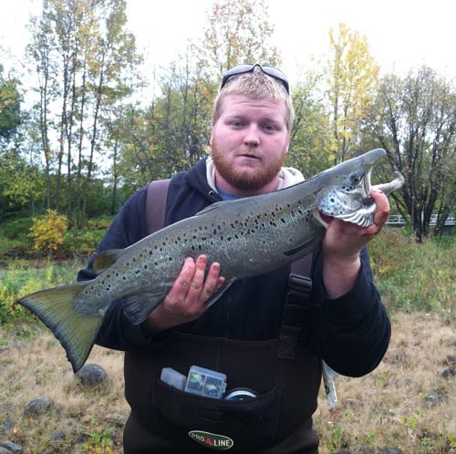 Man in sweatshirt and fishing vest holding salmon