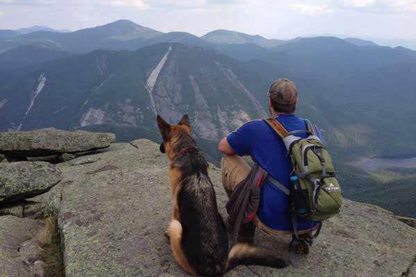 Hiker and german shepherd enjoy view from rocky ledge