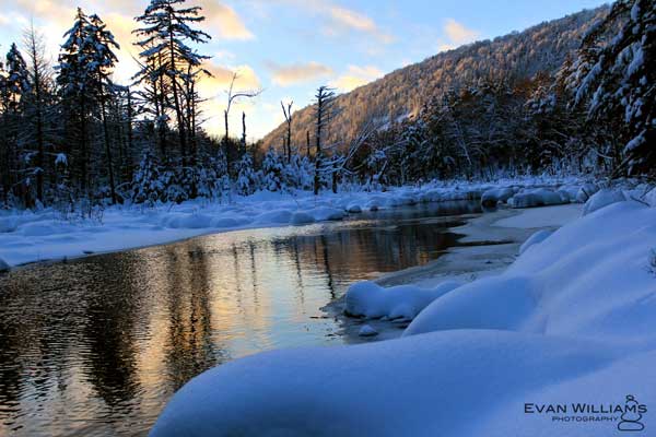 Sunset over a river lined with snow and trees