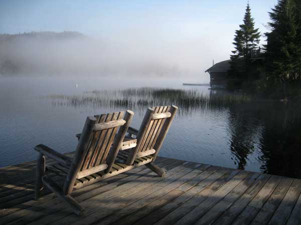 Adirodnack chairs sitting on a dock overlooking a foggy lake