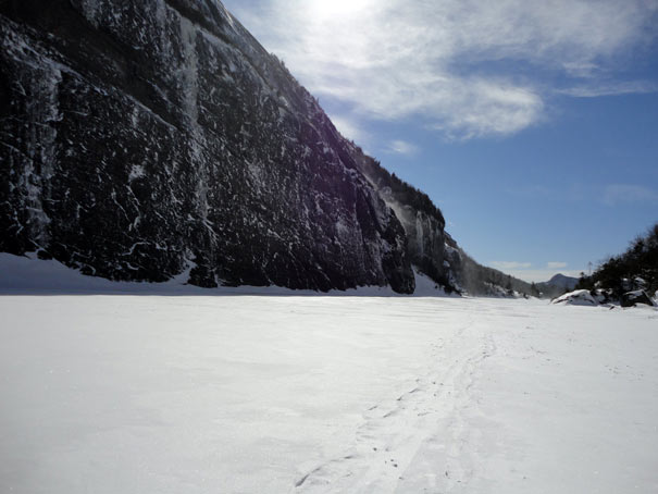 Hiking trail covered in snow next to a sheer cliff wall