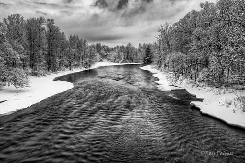 rippling water of the Saranac River in winter lined by snow covered trees