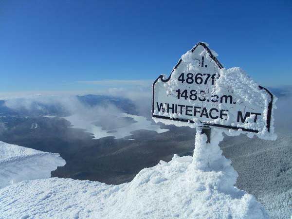 Snowy sign marking summit of whiteface mountain overlooking Lake Placid