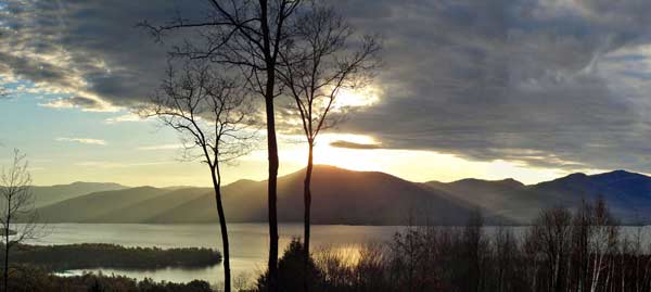 sun rays shining onto lake george from behind a mountain