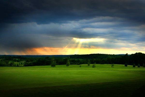 sun rays breaking through a cloudy sky over a green field