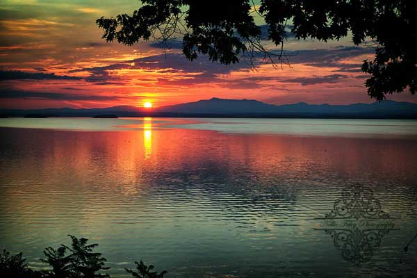 sun rising behind the mountains across a lake