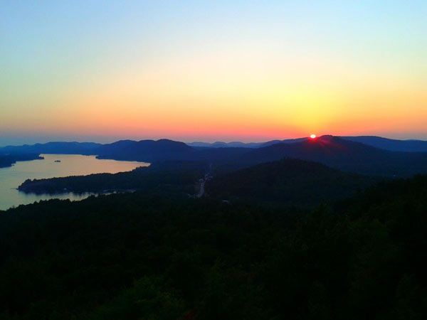 sun rises over mountain peaks near a lake