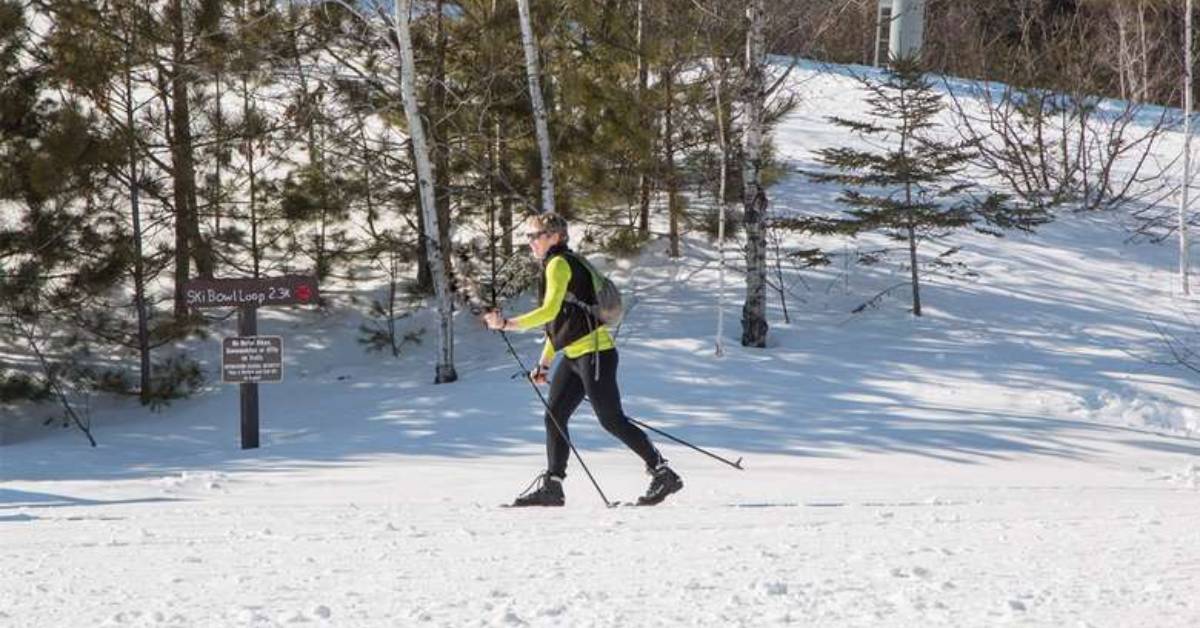 a woman cross country skiing across snowy trail with a sign nearby