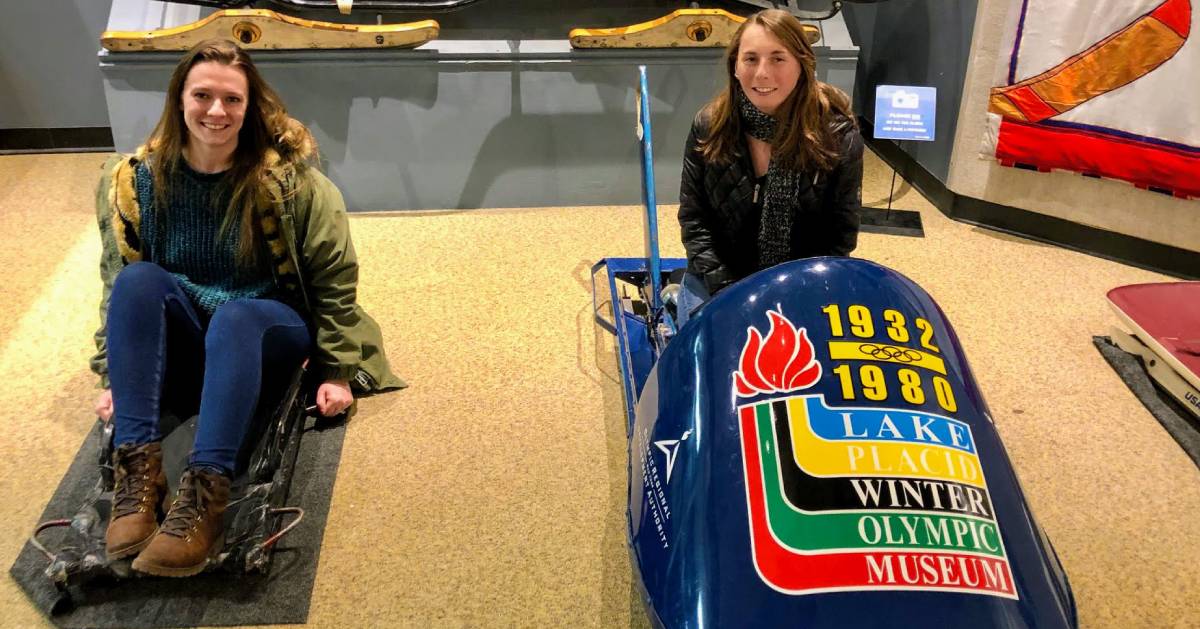 two women posing on bobsleds at museum