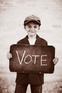 young boy in newsboy cap and suit jacket holding sign that reads 'vote'