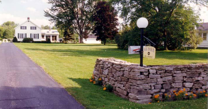 a stone wall by a long driveway leading up to the bed and breakfast