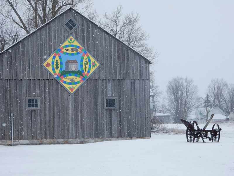 Colorful painted barn quilt displayed on a grey barn in winter in Hammond NY