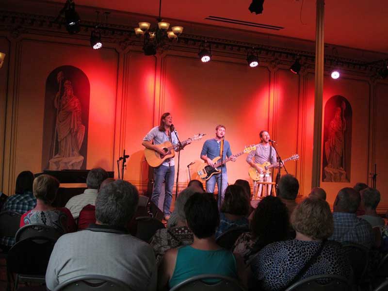 Three men playing music and singing on stage at Pickens Hall